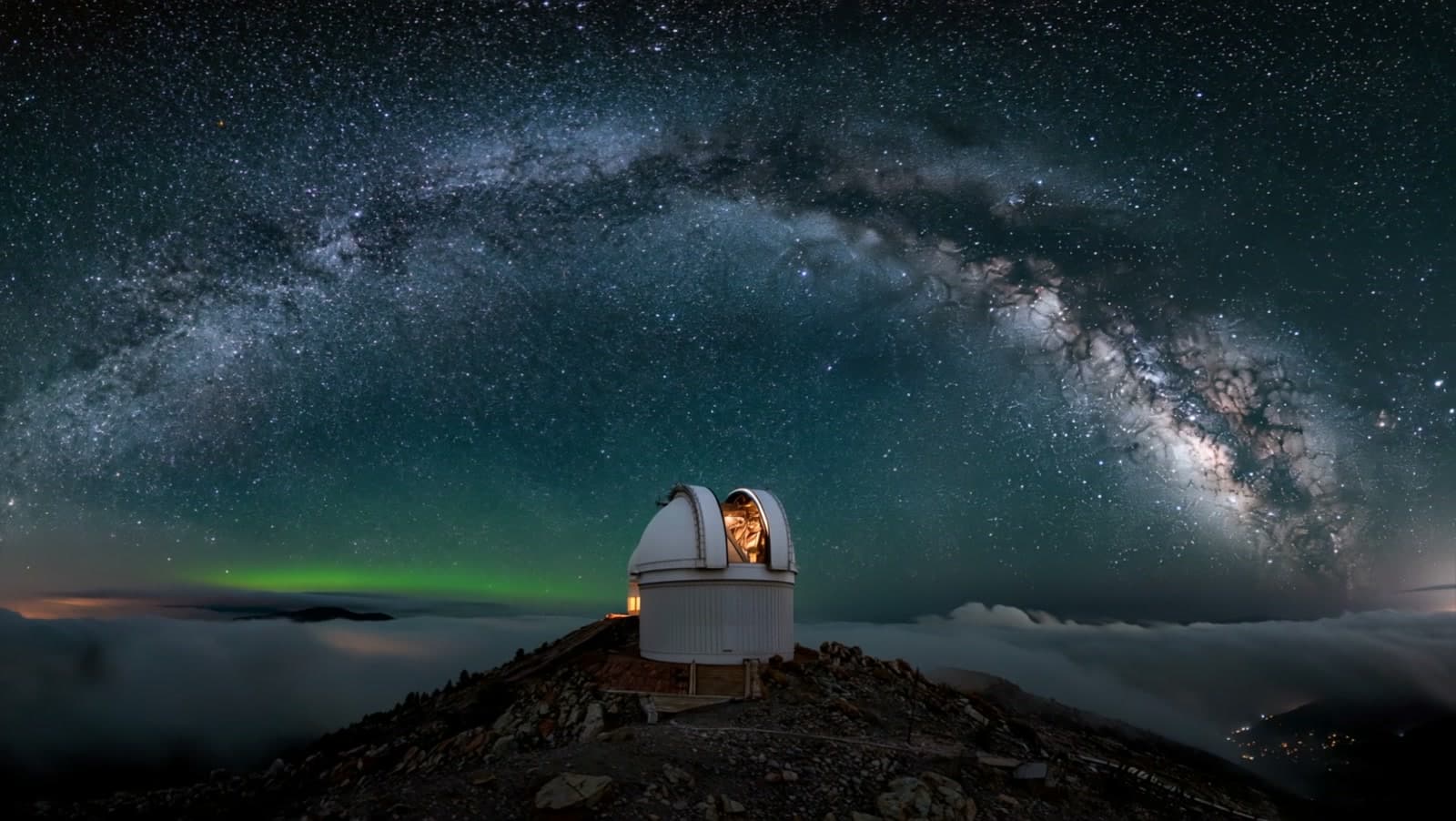 A mountaintop observatory dome under the Milky Way, its open slit glowing faintly warm