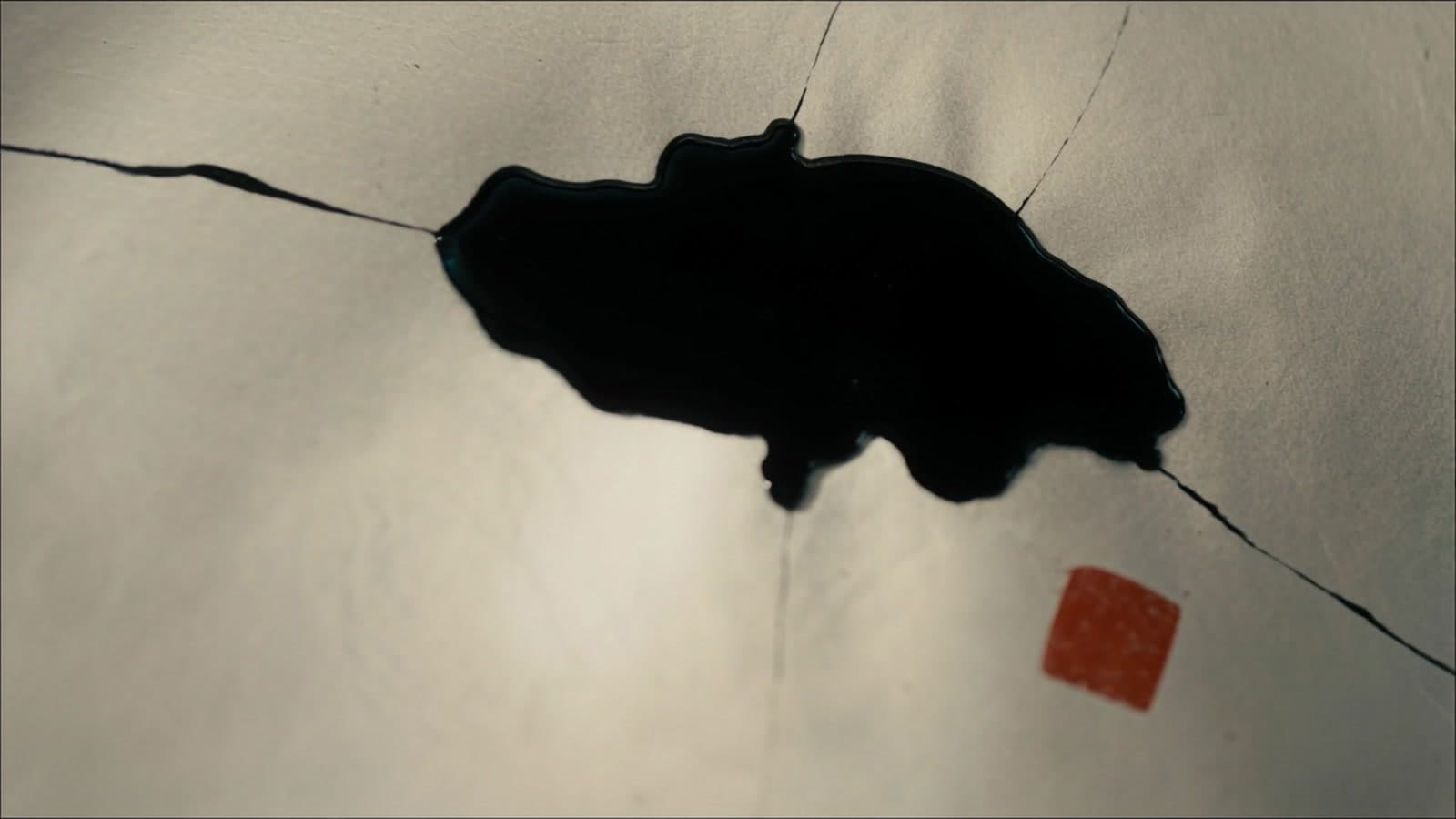 A pool of black ink on warm rice paper with fine cracks of ink running out from it and a small vermilion seal below
