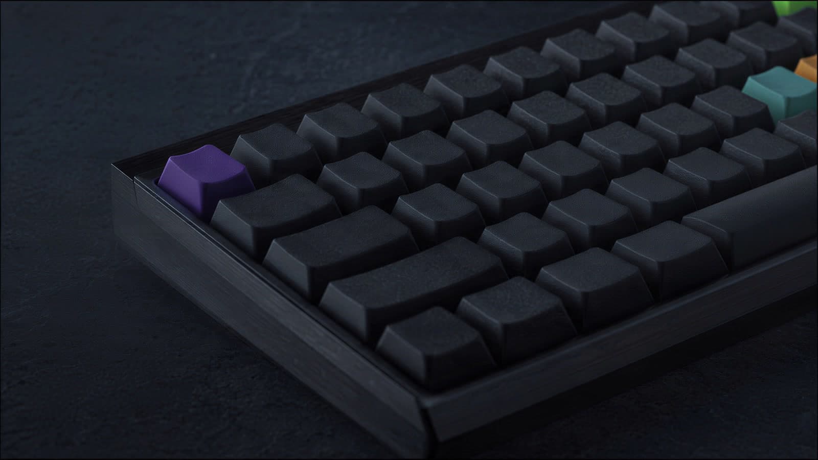 Close-up of a dark mechanical keyboard on a slate desk in low side light, rows of blank charcoal keycaps in a brushed graphite case, one violet key at the near corner and teal, amber and green keys at the far edge