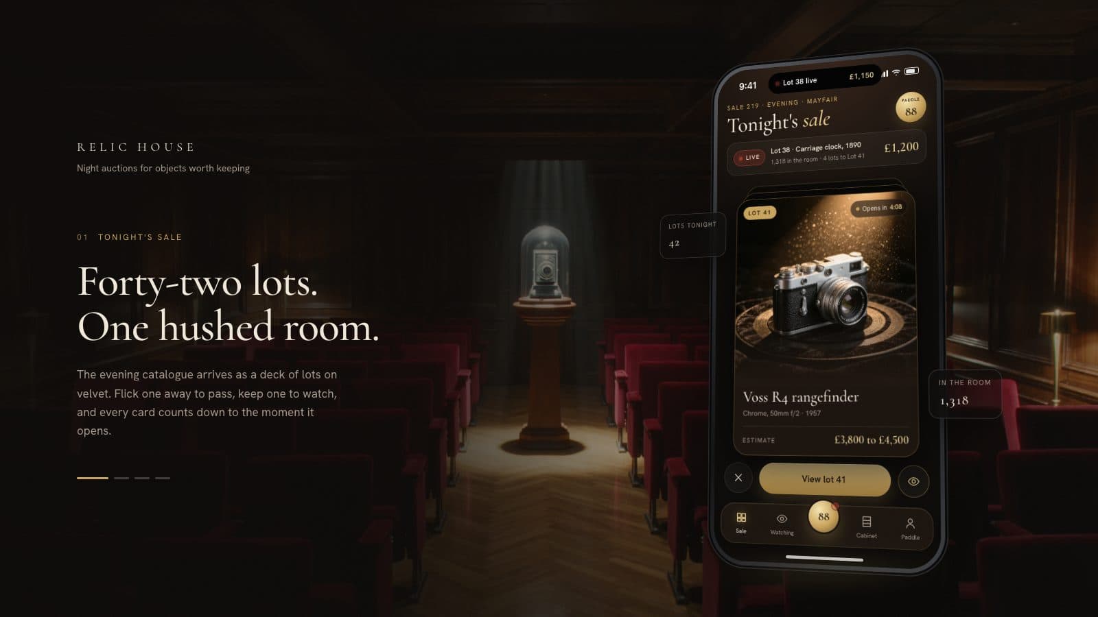 A phone in a dark auction room, showing a vintage chrome camera lot on a spotlit velvet turntable