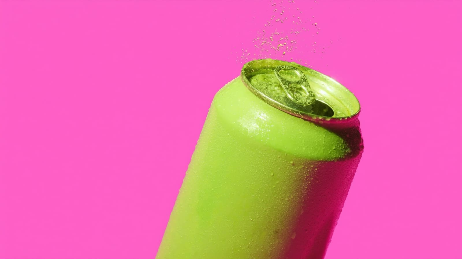 A pistachio green can tipped toward the camera on a hot pink backdrop, fizz spraying up from its open tab